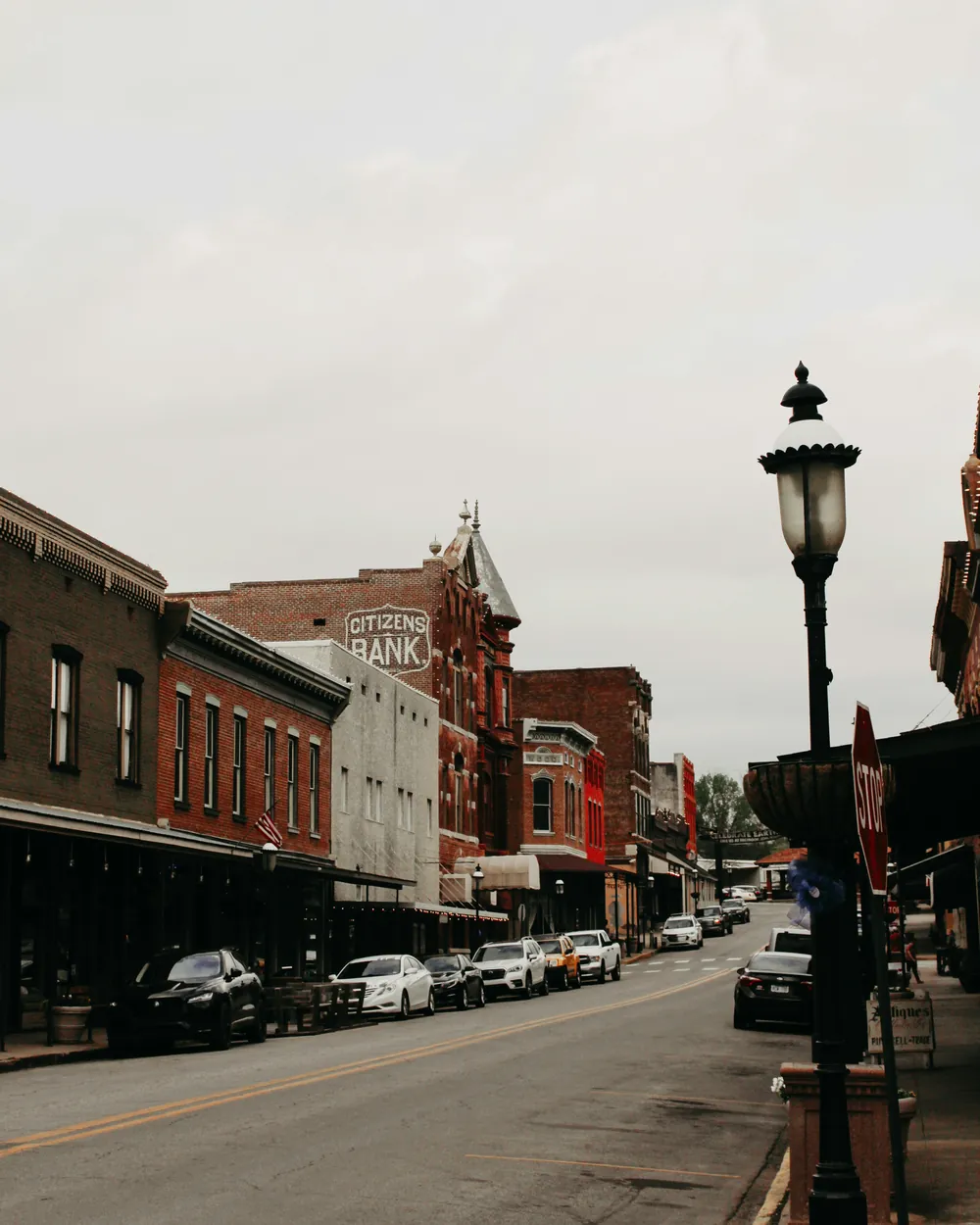 Historic downtown street lined with red brick storefronts and parked cars, with a painted Citizens Bank sign on a brick wall