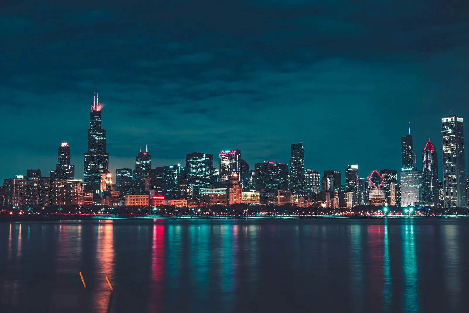 Chicago skyline at night across the water, with lit skyscrapers and red and teal reflections