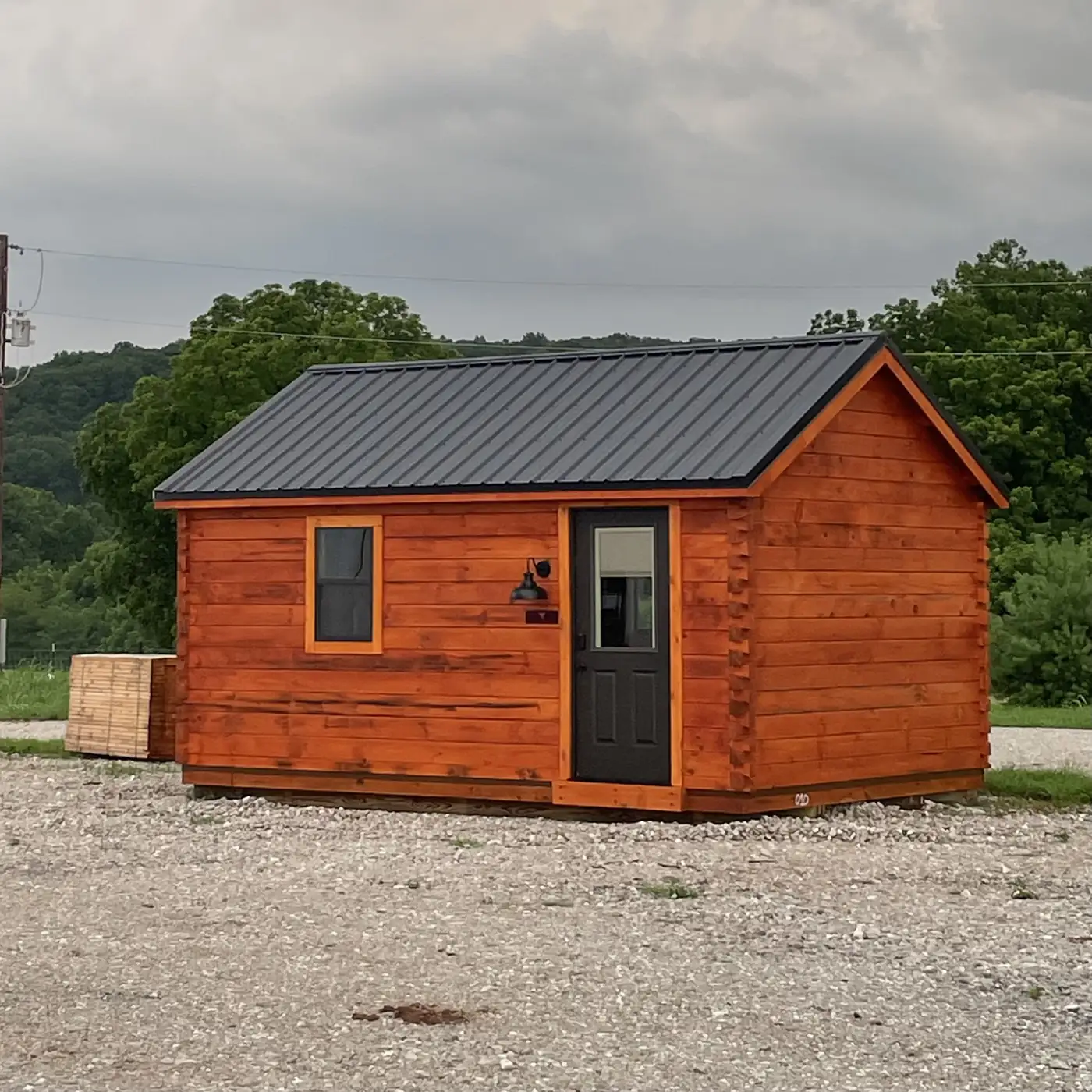 The Cub log cabin with a metal roof, window and black door on a gravel lot
