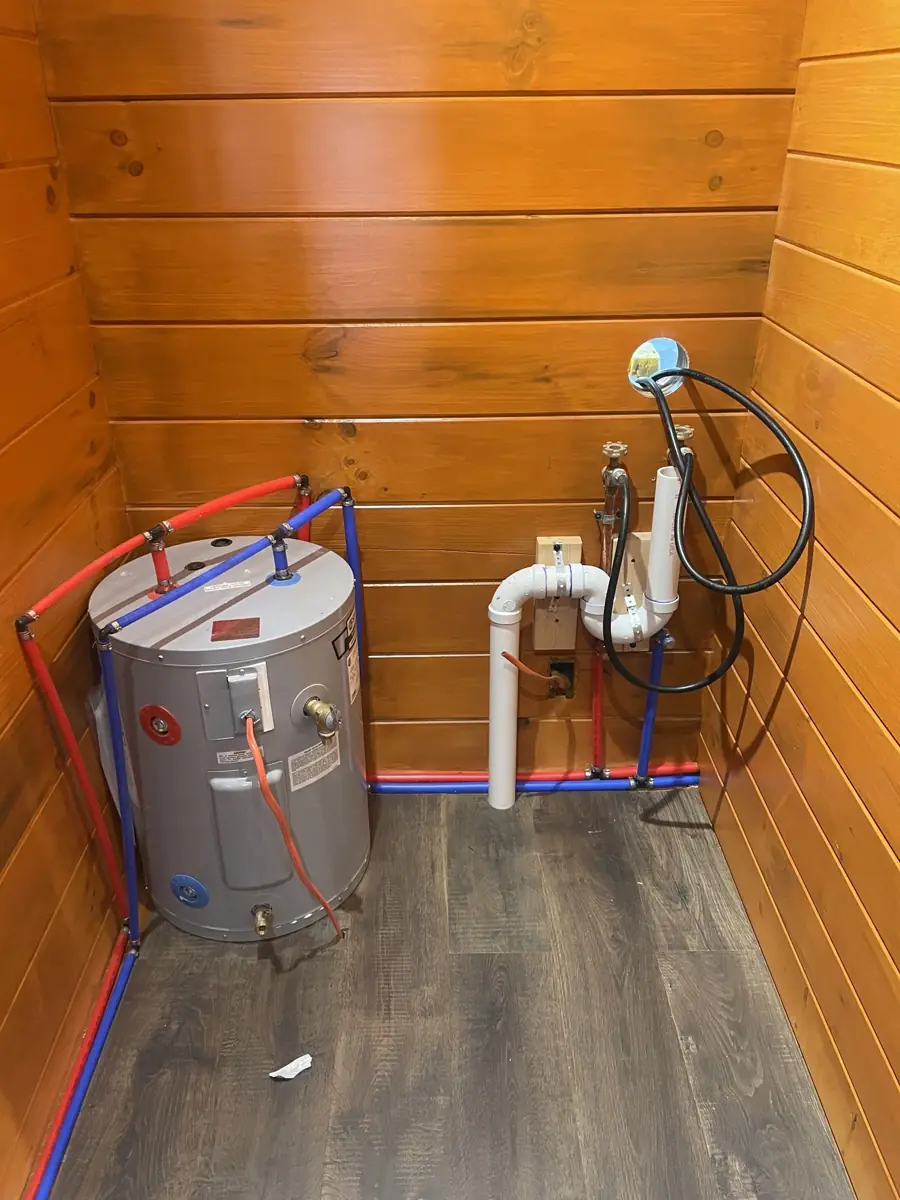 Water heater and plumbing hookups inside The Cub with pine walls and vinyl plank floor