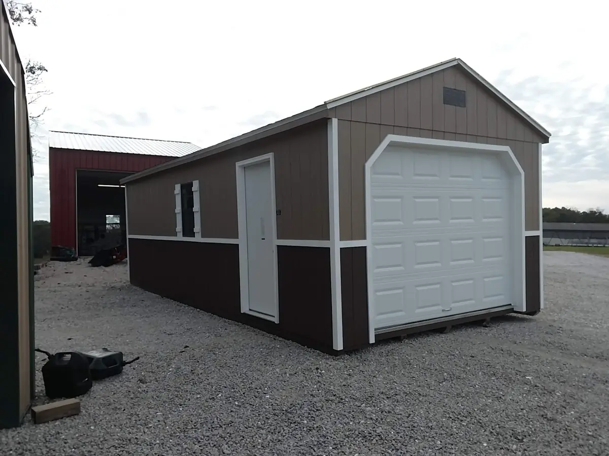 Brown and tan utility garage with a white roll-up door on gravel