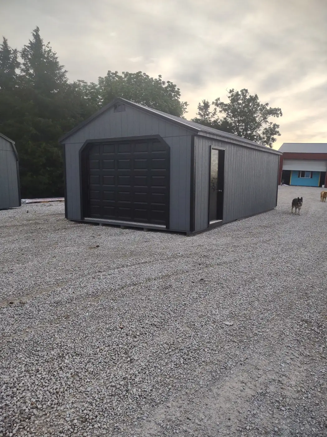 Charcoal utility garage with a black roll-up door on a gravel lot
