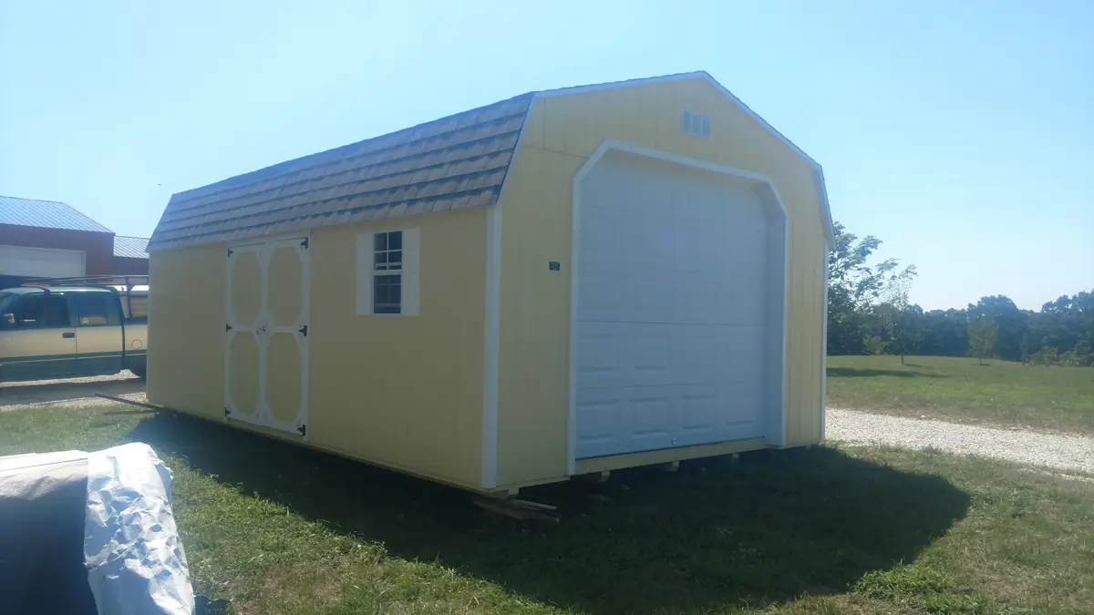 Yellow lofted garage with a barn roof and white roll-up door on a grassy lot