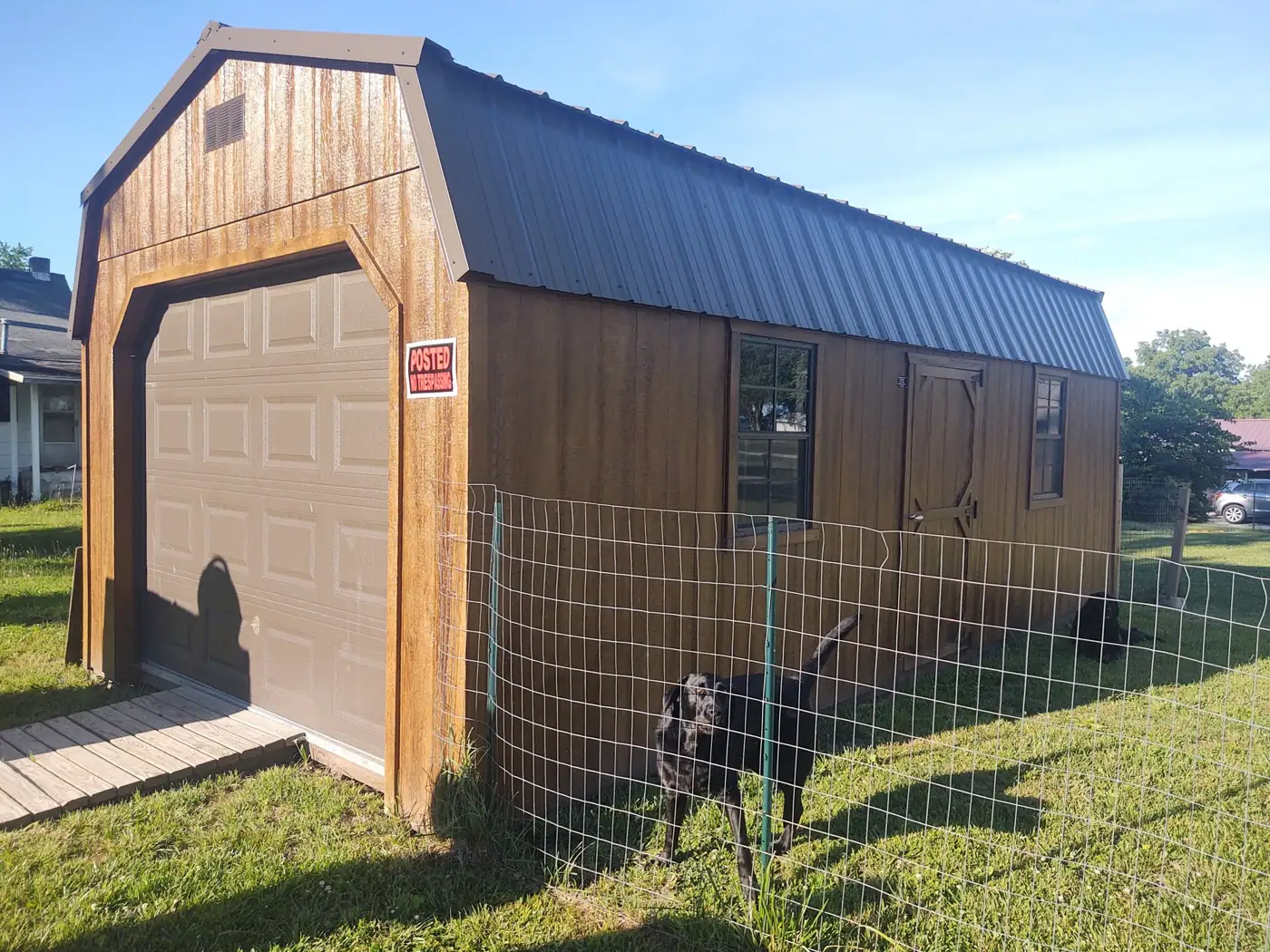 Stained lofted garage with a barn roof and roll-up door beside a fenced yard