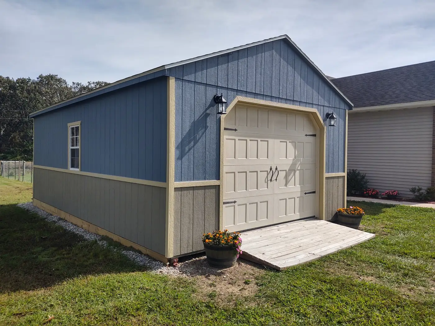 Blue and gray utility garage with a white roll-up door, carriage lights and a ramp