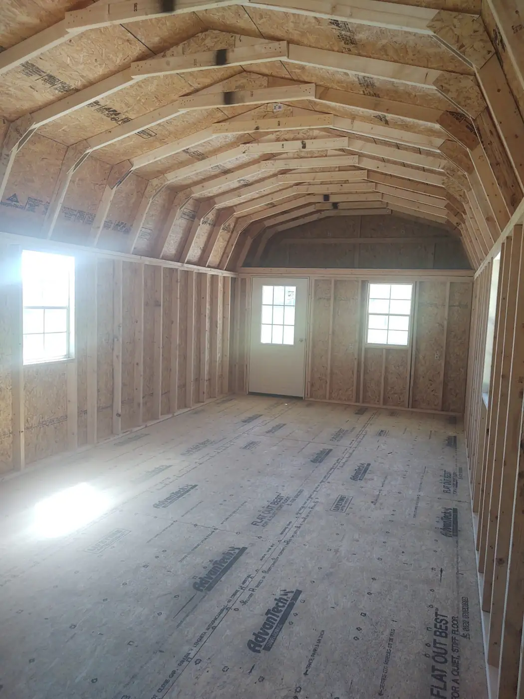 Inside a lofted cabin: open floor, framed walls, overhead loft and two windows