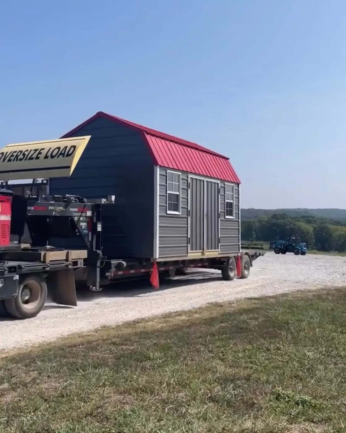 Charcoal lofted barn with a red metal roof loaded on a delivery trailer