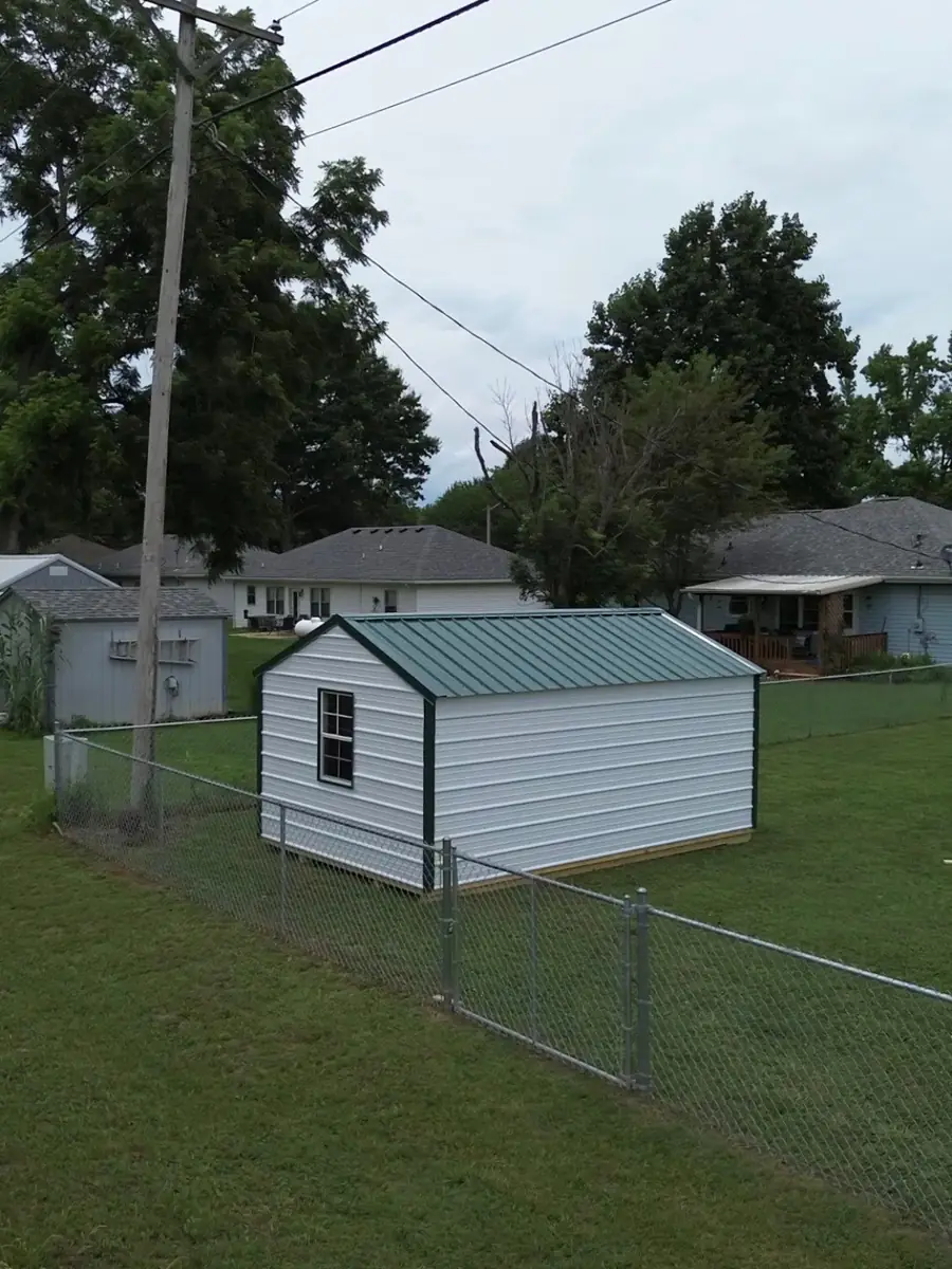 Aerial view of a white utility shed with green trim in a fenced backyard