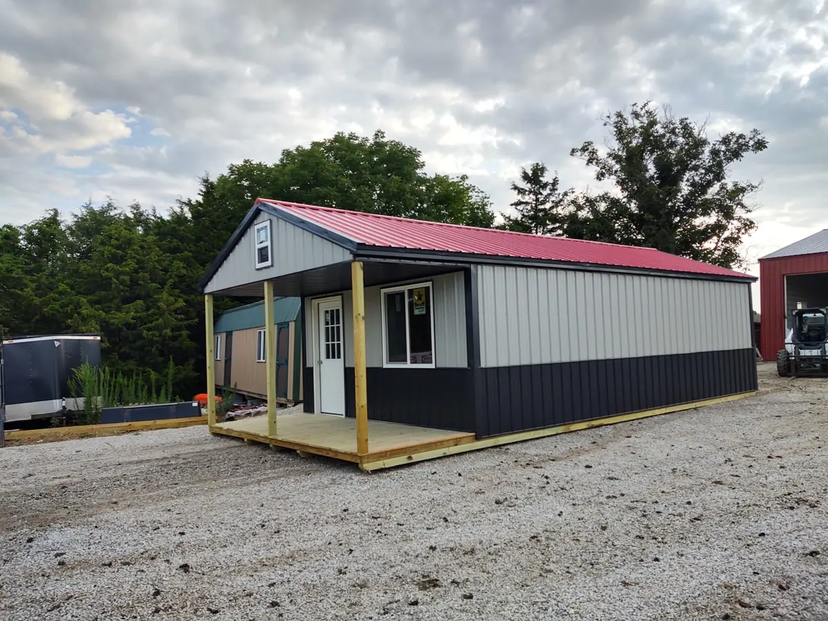 Black and white utility cabin with a red metal roof and a covered porch
