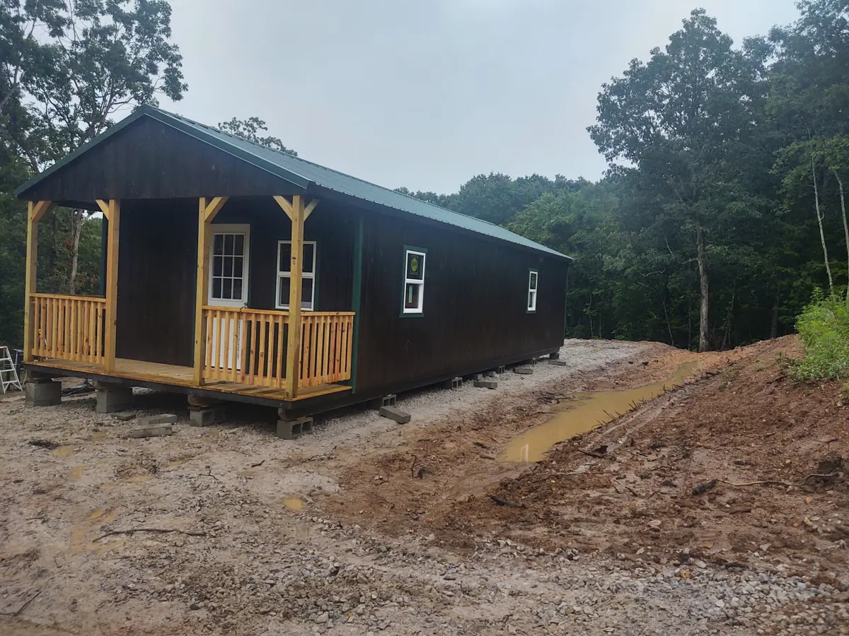 Charcoal utility cabin with a stained porch and railings set on a cleared lot