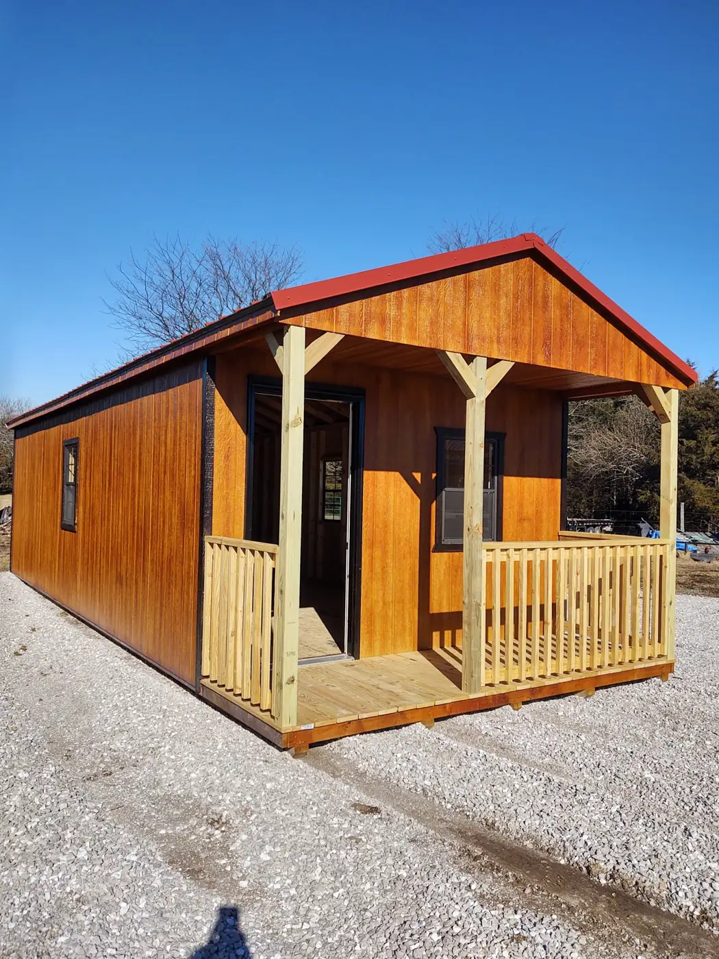 Stained utility cabin with a red metal roof and a covered front porch with wood railings